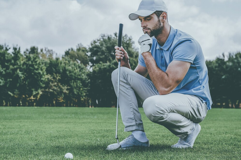 Golfer in a white cap squatting and observing the green.