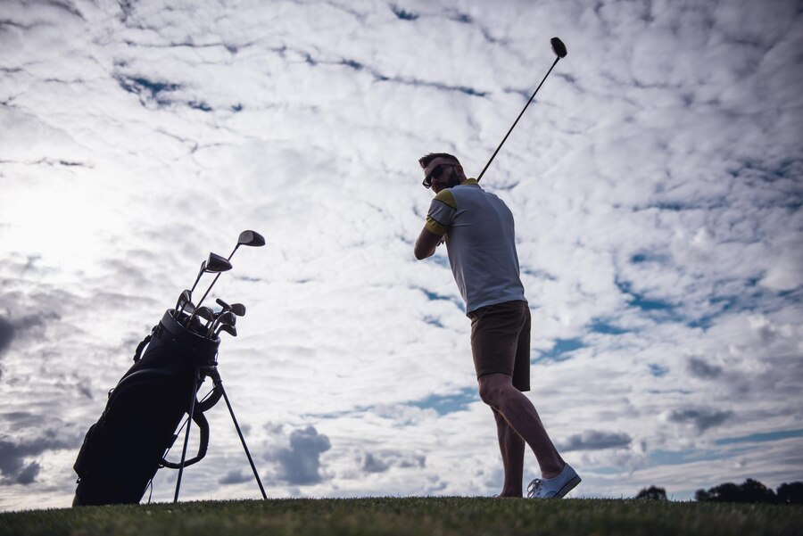 Golfer taking a swing with a cloudy sky background.